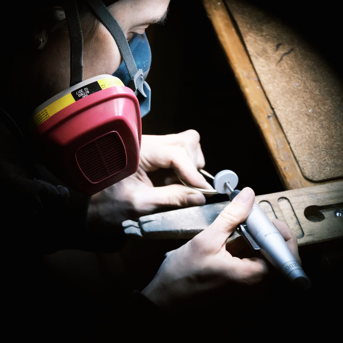 Andrea Pusillo at work in her studio, wearing a respirator and using a jeweler's tool.